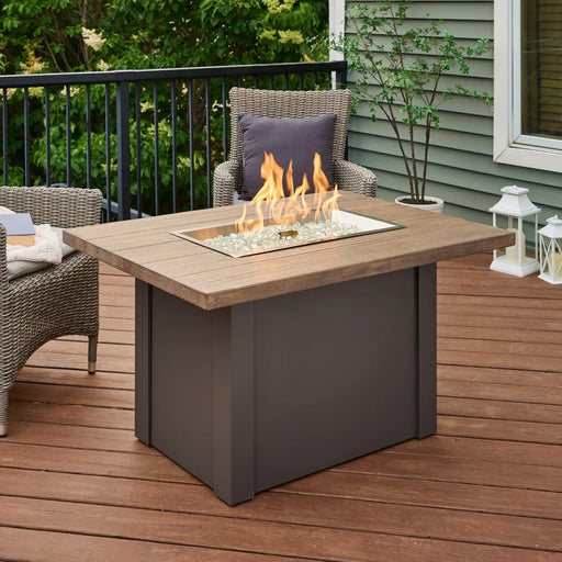 The Fire Pit Table lit with flames, with outdoor seating and decorative elements around it.