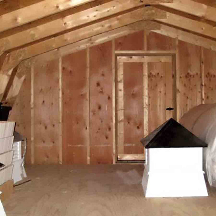 Interior view of a wooden gambrel barn structure with visible trusses and unfinished plywood floors, indicating the precut components of the kit.