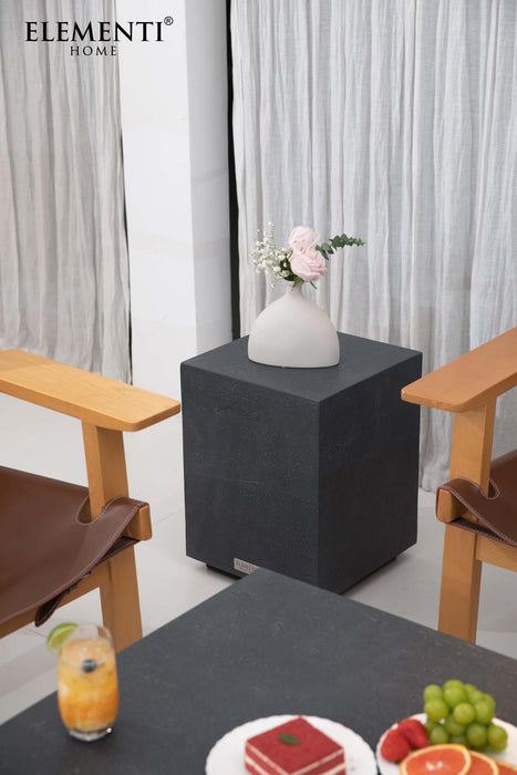 Elementi Colorado Series slate black side table styled in a modern interior setting with neutral curtains and wooden chairs.