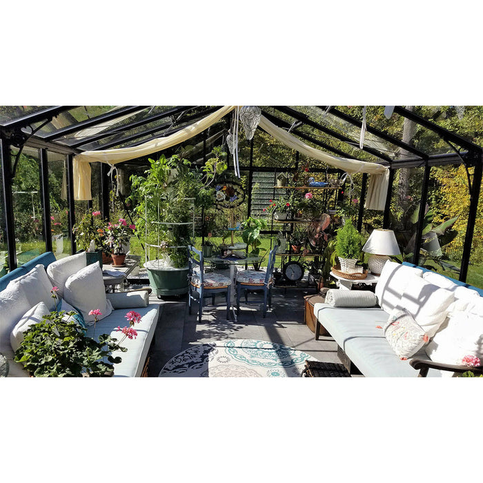 Interior of the Janssens Royal Victorian VI 46 Greenhouse stylishly arranged with an assortment of potted plants, comfortable furniture, and decorative items, creating an intimate space for relaxation and gardening.