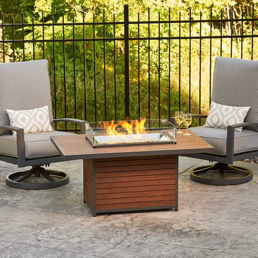 The Fire Pit Table lit with flames, with outdoor seating and decorative elements around it.