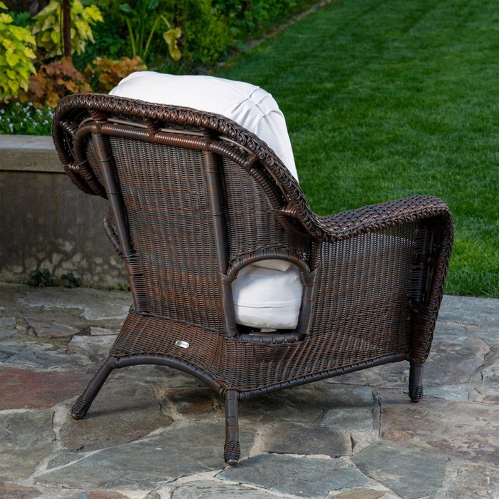 The Tortuga Outdoor Sea Pines 6-Piece Outdoor Wicker Sofa Set in Java features brown wicker chairs with white cushions, elegantly arranged on a stone patio beside a grassy lawn and garden.
