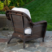 The Tortuga Outdoor Sea Pines 6-Piece Outdoor Wicker Sofa Set in Java features brown wicker chairs with white cushions, elegantly arranged on a stone patio beside a grassy lawn and garden.