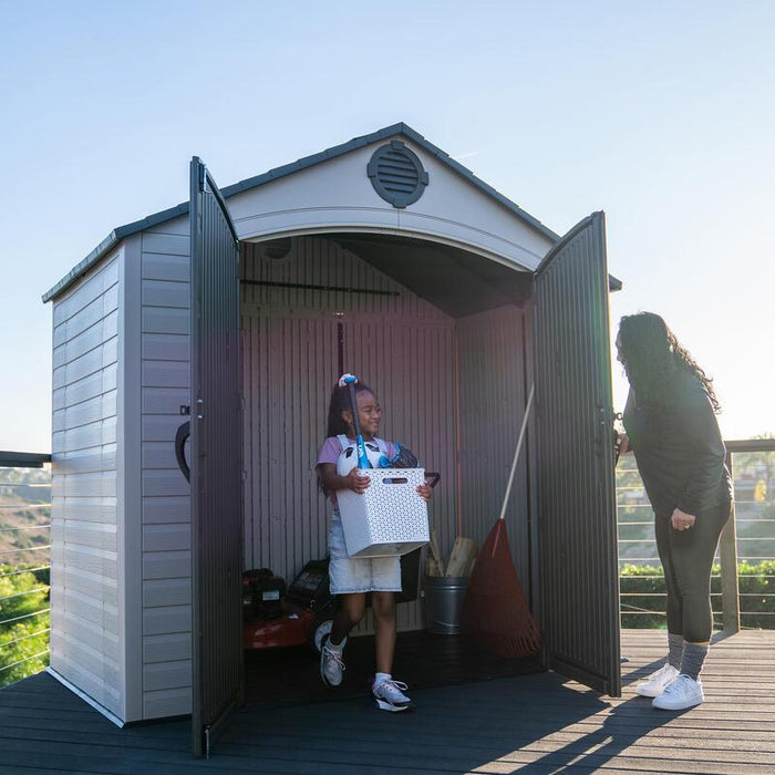 A child and an adult unpacking items in front of the open Lifetime 8 ft x 5 ft Outdoor Storage Shed.
