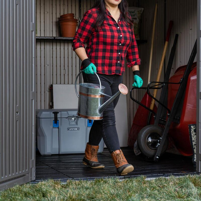 Woman carrying a water can by the open doors of a storage shed