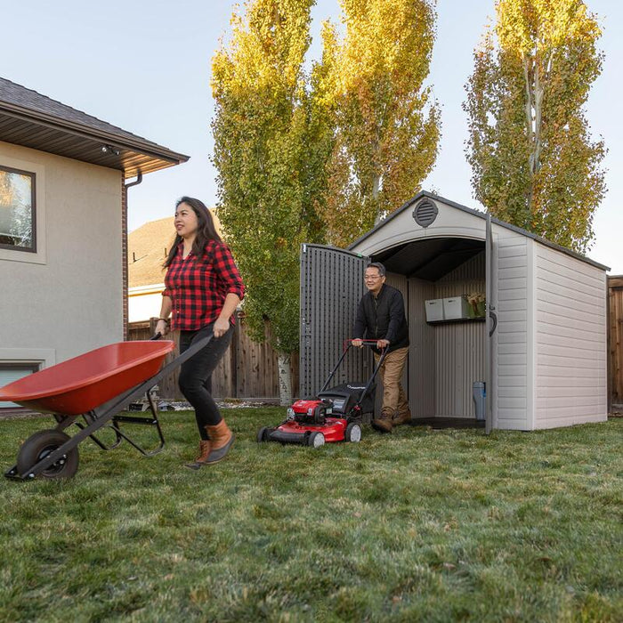A lifestyle image showing two people engaging in gardening activities near the open Lifetime 8 ft x 7.5 ft Outdoor Storage Shed.