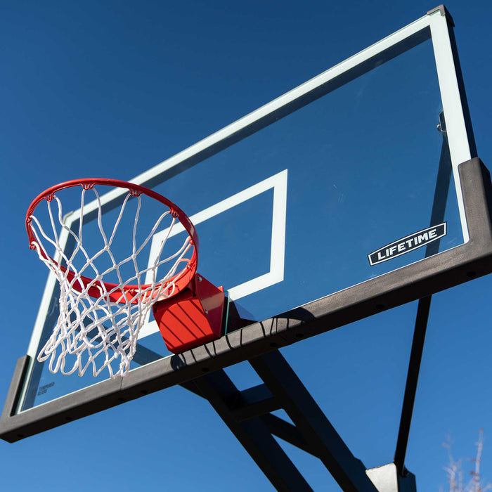 Angled view of the Lifetime 72-Inch Mammoth Bolt Down Basketball Hoop showing the backboard, red rim, and part of the pole against a blue sky.