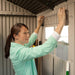 A woman installing a shelf accessory inside the Lifetime 7 x 7 ft Outdoor Storage Shed.