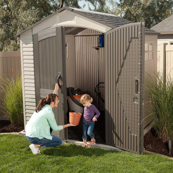 Adult and child opening the Lifetime 7 x 7 ft Outdoor Storage Shed with gardening tools visible inside.