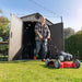  Man pushing a lawn mower out of the open Lifetime 8 x 17.5 ft Outdoor Storage Shed in a residential garden.