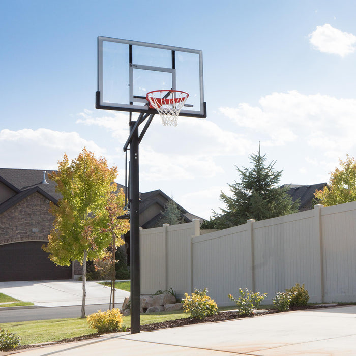 Lifetime Adjustable In-Ground Basketball Hoop with a 54-inch acrylic backboard installed in a residential driveway with a clear sky and house in the background.