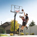 An action shot of a player shooting a basketball towards the Lifetime Adjustable In-Ground Basketball Hoop on a sunny day with residential background.