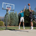 Two players in action playing basketball with the Lifetime Adjustable Bolt Down Basketball Hoop, 60-Inch Tempered Glass in a driveway setting.