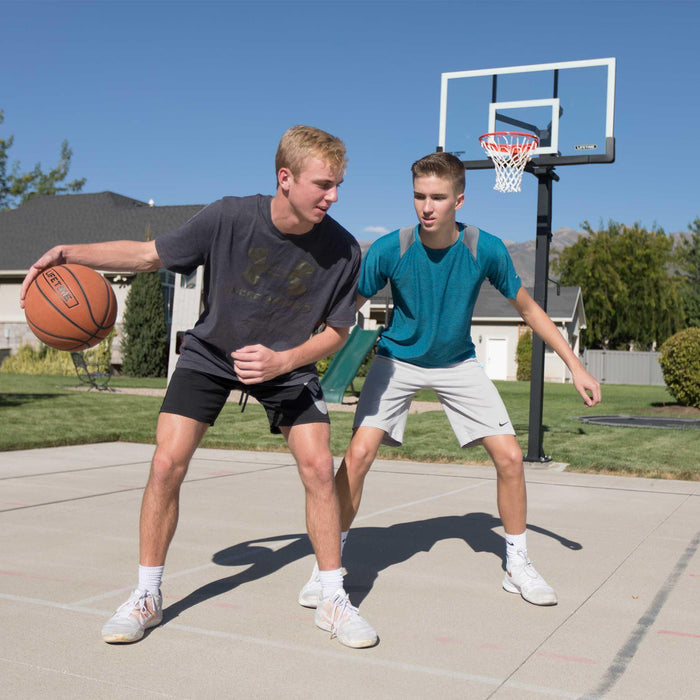 wo men playing one-on-one basketball with the Lifetime Adjustable Bolt Down Basketball Hoop in the background.