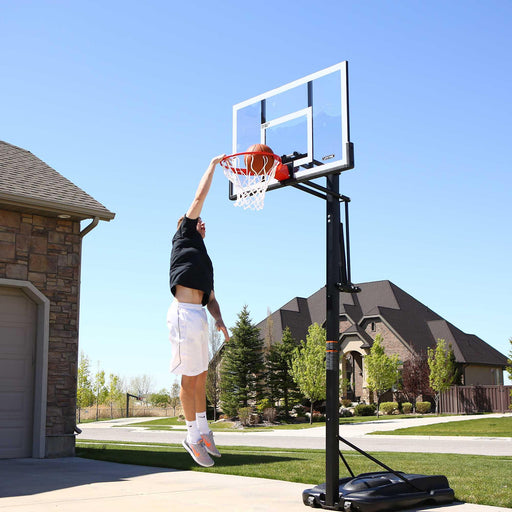 Man performing a dunk on a Lifetime Adjustable Portable Basketball Hoop with a clear sky background.