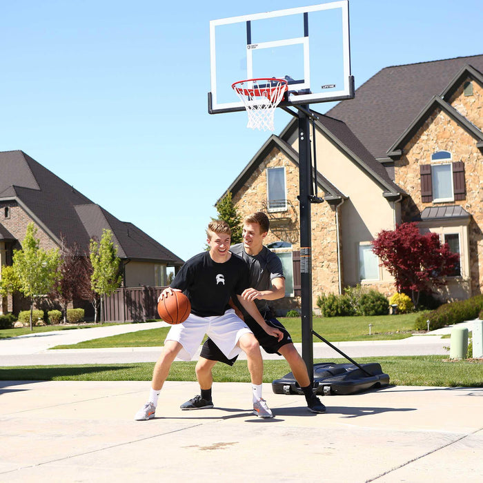 Two boys in casual wear dribbling and playing basketball with the Lifetime 54-Inch Portable Hoop in their driveway.