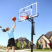 Girl in blue shirt shooting a basketball at a Lifetime Adjustable Portable Hoop on a sunny day.