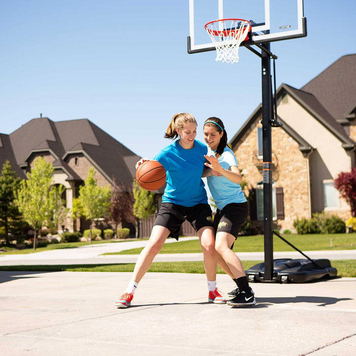 Two girls in athletic wear playing basketball, with one defending, in a driveway with the Lifetime Portable Basketball Hoop.