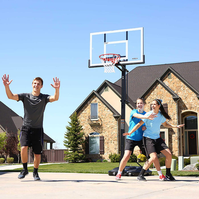 Teenagers playing basketball with a Lifetime Adjustable Portable Basketball Hoop in the background.