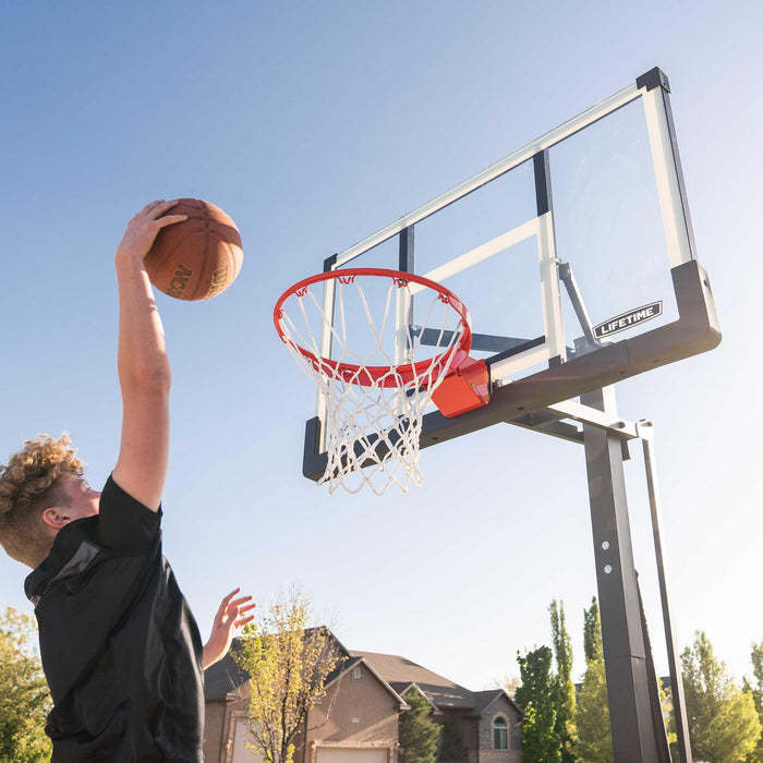 Player dunking basketball in a Lifetime Adjustable Portable Basketball Hoop with a 54-inch tempered glass backboard.