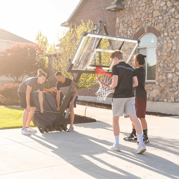A group of people setting up the Lifetime Adjustable Portable Basketball Hoop with a 54-Inch Tempered Glass on a driveway.
