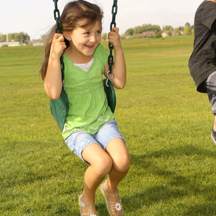 A young girl in a green shirt smiling while sitting on a swing at the playset.