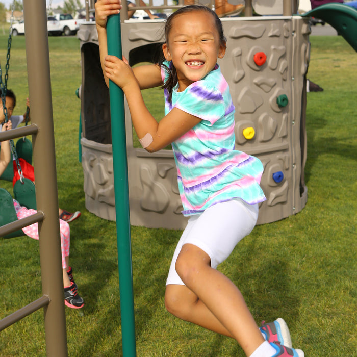 A smiling girl in a tie-dye shirt climbing on the playset with other children around.