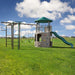 The Adventure Tower Deluxe playset set up outdoors on a grassy field with clear skies above.