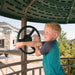 A boy playing with a steering wheel feature on the Lifetime Adventure Tower Playset with houses in the background.