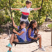 Three children smiling on a black spider swing attached to the Lifetime Adventure Tower Playset with a green and natural background.