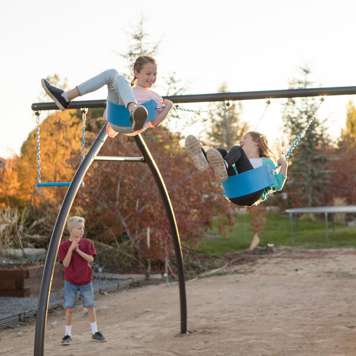 Two children swinging on blue swings at dusk, with another child watching, as part of the Lifetime Adventure Tower Playset.