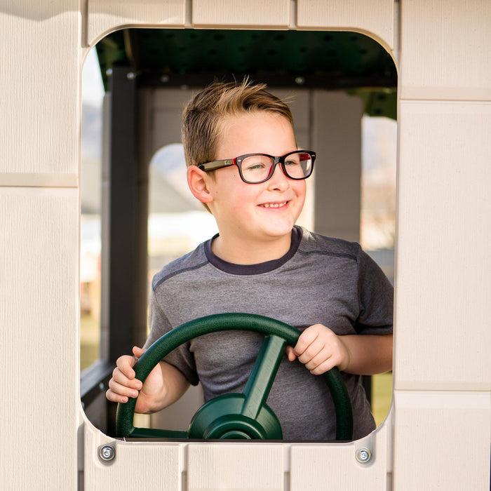 A boy holding the steering wheel at the playset's driving station with a joyful expression.
