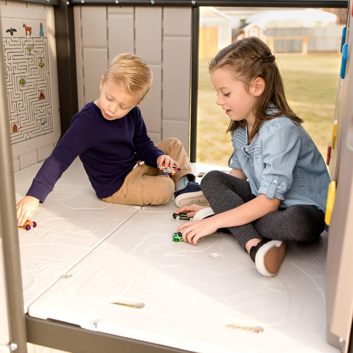 Two children playing with toy cars on the integrated car map of the playset's storefront.