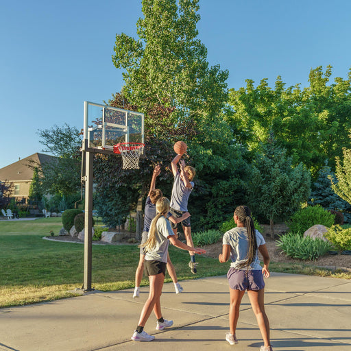 An action shot of a basketball game with a player making a jump shot at the Lifetime Crank Adjust Bolt Down Basketball Hoop in a home setting.