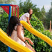 Children enjoy a fun descent on the yellow slide of the Lifetime Big Stuff Deluxe Swing Set, with their laughter and enjoyment captured in the moment.