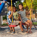 A boy in a checked shirt and two other children enjoy the swing and climbing features of the Lifetime Big Stuff Deluxe Swing Set in primary color scheme.