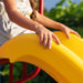 A close-up of a child's hands on the yellow slide of the Lifetime Big Stuff Deluxe Swing Set, focusing on the secure design and playful color.
