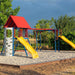 Wide-angle view of the Lifetime Big Stuff Deluxe Swing Set featuring a red clubhouse, blue and red swings, yellow slides, and a rock-climbing wall, set in a sand-covered play area.