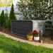 The Lifetime Modern Outdoor Storage Deck Box placed in a garden setting next to flowers and a garden light.