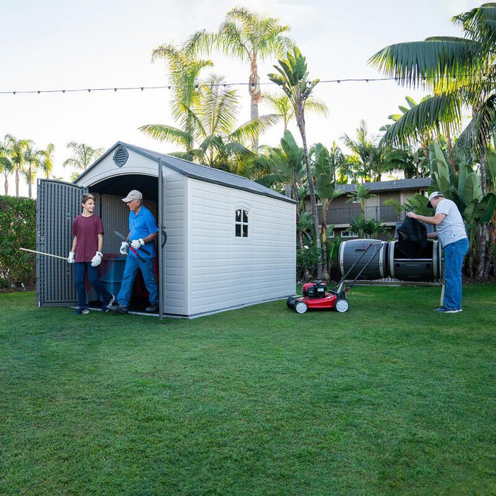 A family utilizing the Lifetime 8 ft x 12.5 ft Outdoor Storage Shed, with tools and garden equipment being moved in or out.