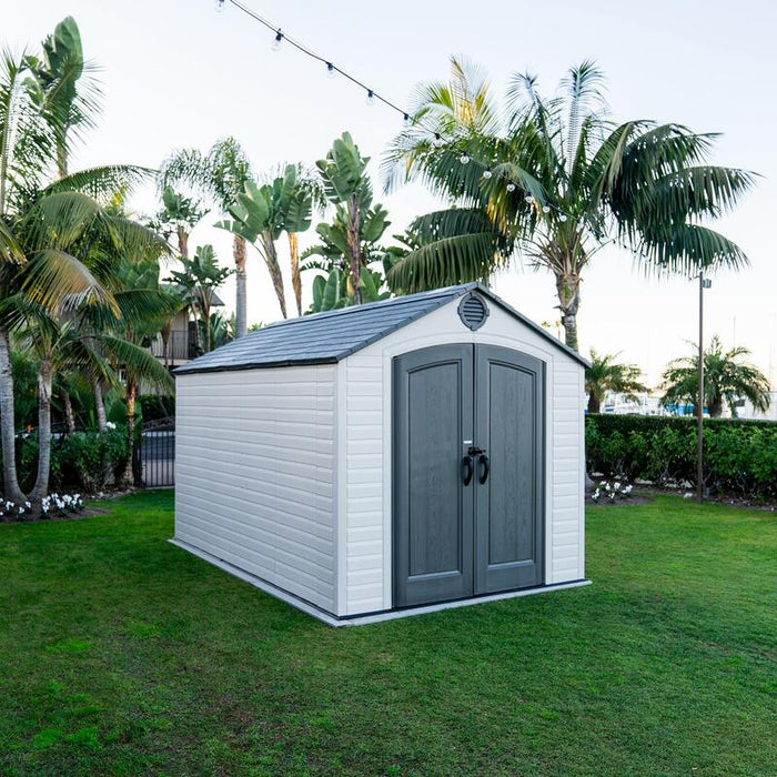 Full view of the Lifetime 8 ft x 12.5 ft Outdoor Storage Shed during dusk with ambient outdoor lighting, showcasing the shed's aesthetics in an evening setting.