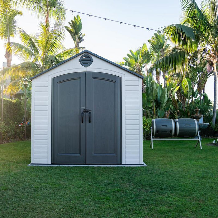 Full exterior view of the Lifetime 8 ft x 12.5 ft Outdoor Storage Shed in a backyard setting, complemented by lush greenery.
