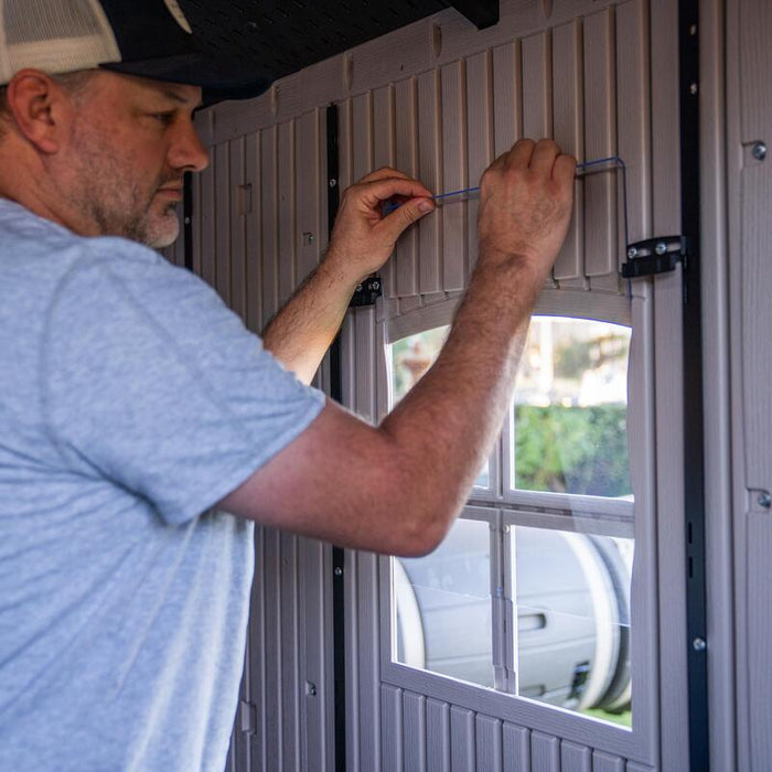 A person installing window glass of the Lifetime 8 ft x 12.5 ft Outdoor Storage Shed, showing the interior setup.
