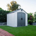 Lifetime 8 ft x 7.5 ft Outdoor Storage Shed placed on a grassy area in a garden setting, showing the side and front of the shed.