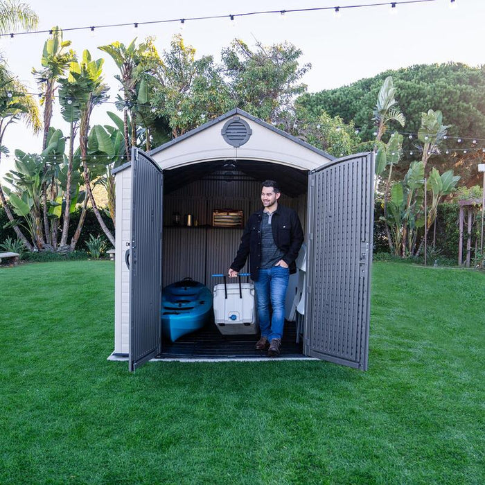 Man carrying a white cooler out of the Lifetime 8 Ft. x 15 Ft. Outdoor Storage Shed with the door open.