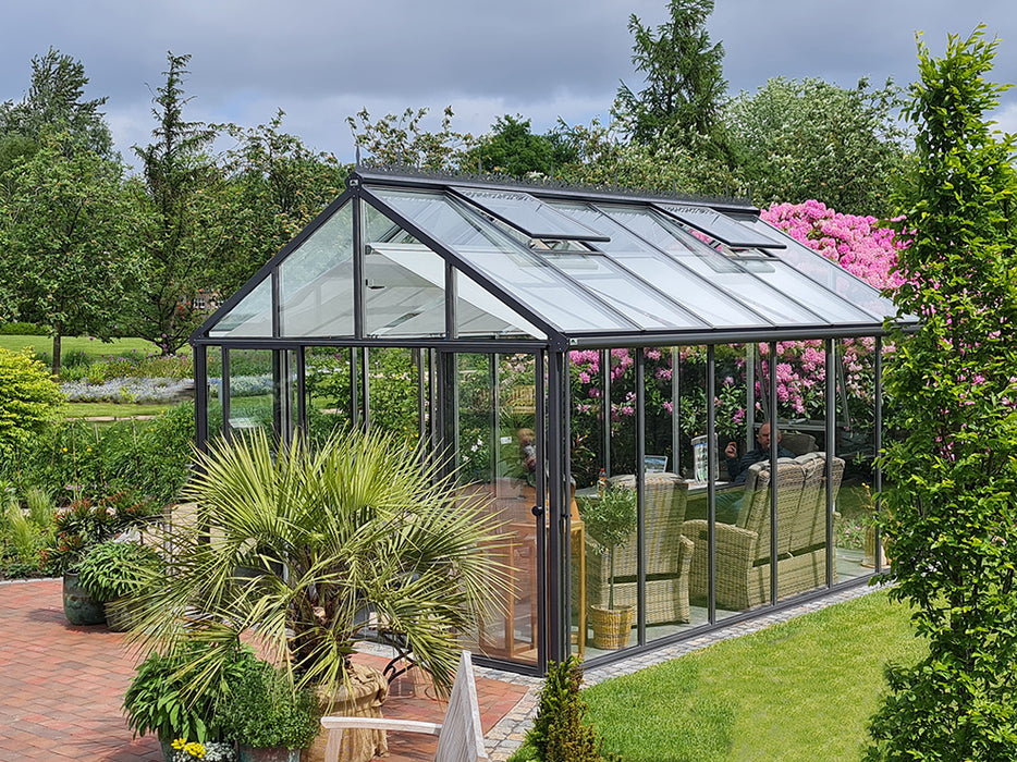 A fully assembled livingten greenhouse with an open door, revealing a furnished interior with dining chairs and table.
