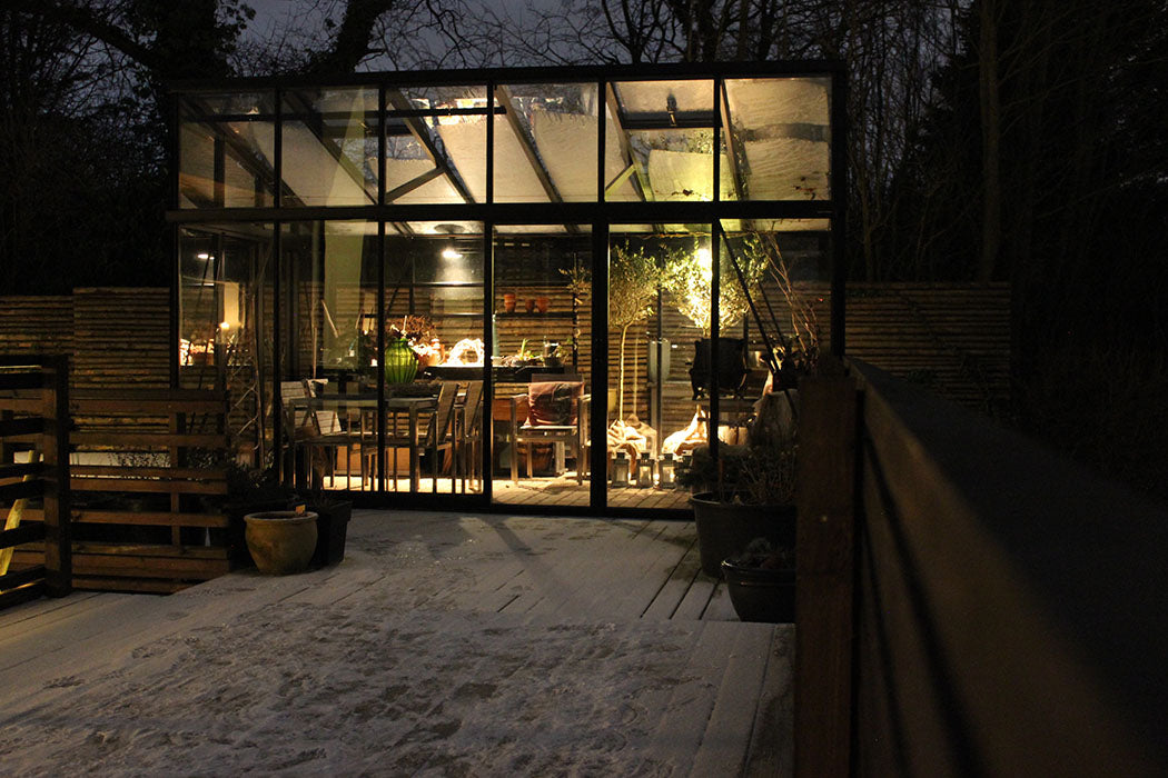 Exaco Janssens M23 modern greenhouse illuminated at night, showcasing the sloping roof and warm interior against a snowy backdrop.