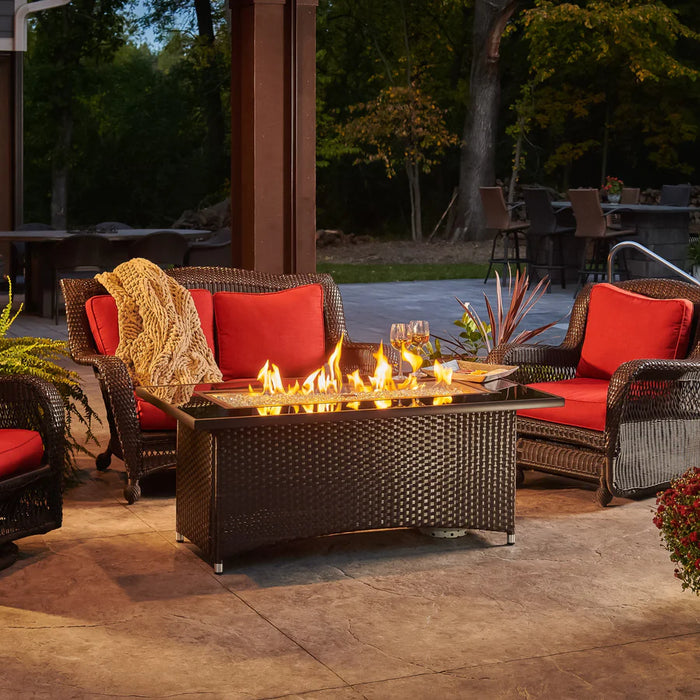 The Fire Pit Table lit with flames, with outdoor seating and decorative elements around it.