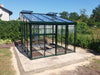 Modern Exaco Janssens M23 greenhouse for vegetables, with a sloping roof, situated in a vibrant garden ready for planting.