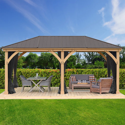 A luxurious outdoor wooden gazebo with a dark metal roof, featuring an integrated mosquito mesh kit. The gazebo is set against a lush garden backdrop, providing a comfortable outdoor seating area with a dining set and lounge furniture.